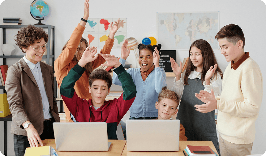 Students and educators celebrating around laptops in a classroom, representing collaborative learning and special education support